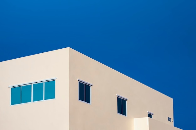 Blaue Glasfenster auf hellgelbem Bürogebäude gegen blauen klaren Himmel in perspektivischer Seitenansicht