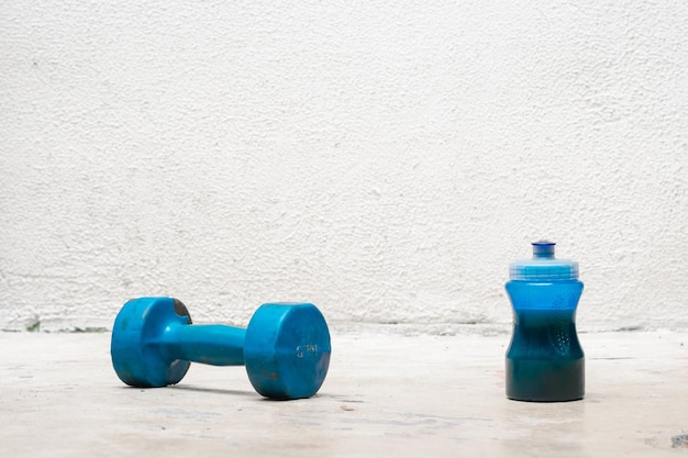 Blaue Hantel und Flasche mit Wasser auf dem Boden verwendet staubigen und verlassenen weißen Hintergrund