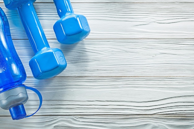 Blaue Hanteln der Wasserflasche auf dem Sporttrainingskonzept des hölzernen Brettes.