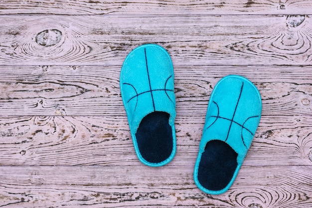 Blaue Hausschuhe auf einer schönen Holzwand. Bequeme Heimschuhe. Flach liegen.