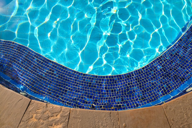 Blaue Kacheln des Whirlpools im blauen Wasser des Swimmingpools und Reflexionseffekt des Sonnenlichts