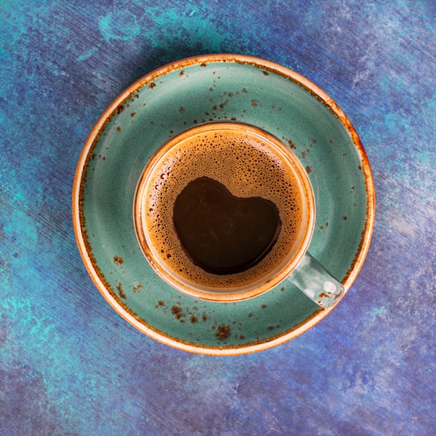 Blaue Kaffeetasse mit der Herzform gemacht vom Schaum auf blauem hölzernem Hintergrund.
