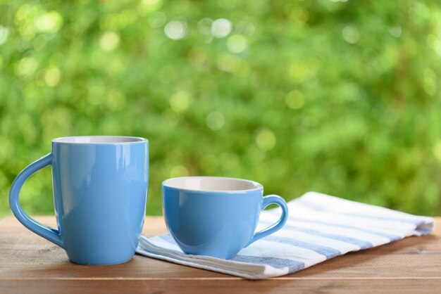 Blaue Kaffeetasse und Nepkin auf Holztischplatte mit grünem unscharfem Hintergrund