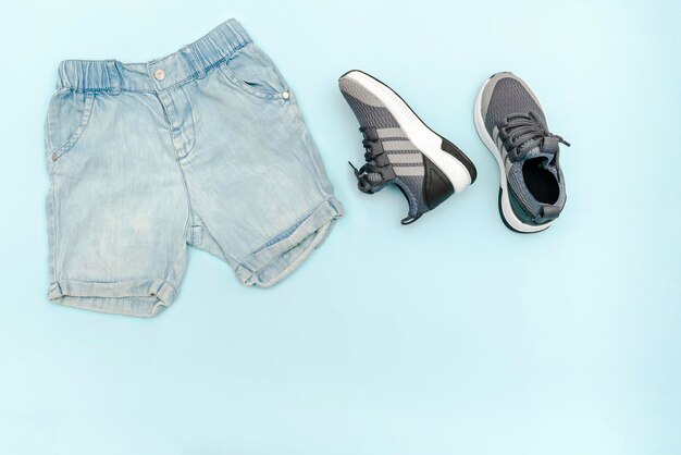 Blaue Kleidung und Accessoires für Sommerbabys mit Jeans-Shorts, Turnschuhen, moderne Mode für Kinder, Set mit Kinderkleidung für Frühling oder Sommer, flache Lage, Draufsicht, Overhead-Mockup mit Kopierbereich