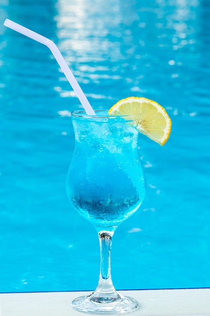 Blaue Lagune in einem Glas mit einem Strohhalm und einer Zitronenscheibe. Sommer süßer Cocktail am Pool.