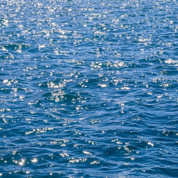 Blaue Meereswellen im Sonnenschein leuchten als Oberflächenhintergrund-Sommerferienkonzept