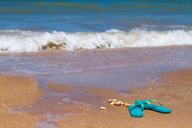 Blaue Pantoffeln stehen im Sand an der Küste