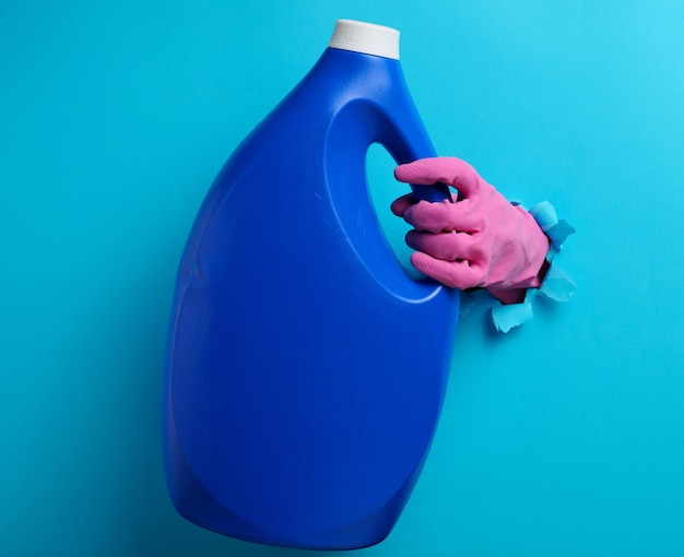 Blaue Plastikflasche mit flüssigem Waschmittel in einer weiblichen Hand auf blauem Hintergrund ein Teil von
