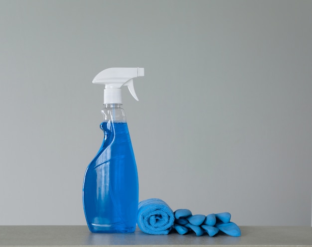 Blaue Reinigungssprühflasche mit Plastikzufuhr, Ringelblumen und Stoff für Staub auf grauem Hintergrund