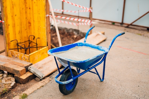 Blaue saubere neue Schubkarre für Zement. Den ersten Schaufelzement in das Fundament auf den Bau des Hauses legen.