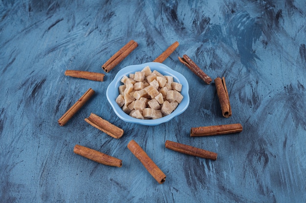 Foto blaue schüssel mit braunen zuckerwürfeln und zimtstangen auf blauer oberfläche.