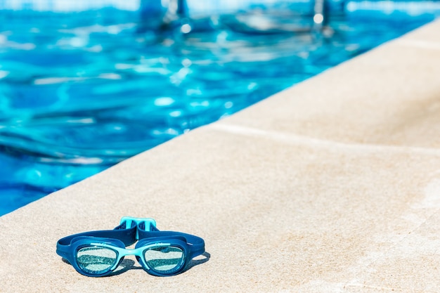 Blaue Schwimmbrille am Rand des Beckens, in der unteren linken Ecke, mit dem blauen Wasser in der Ferne