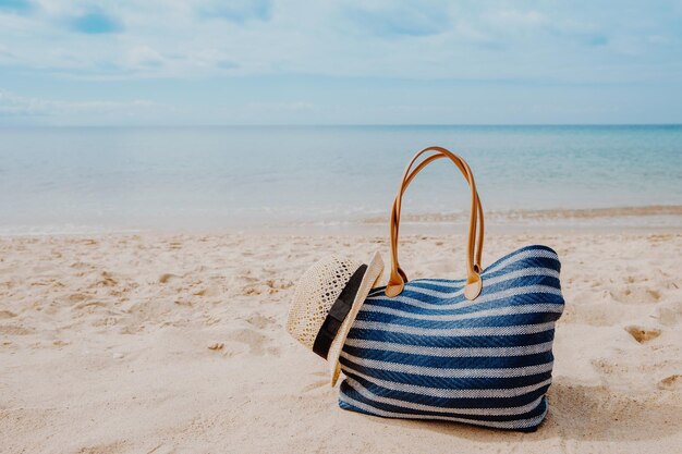 Blaue Strandtasche mit Hut am Sandstrand mit den Sommerferien im Hintergrund des blauen Himmels