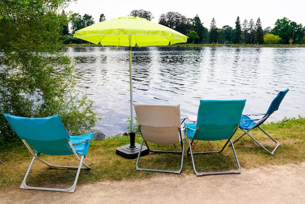 Blaue Stühle, Regenschirm und Tisch aus Metall außen am Flussufer