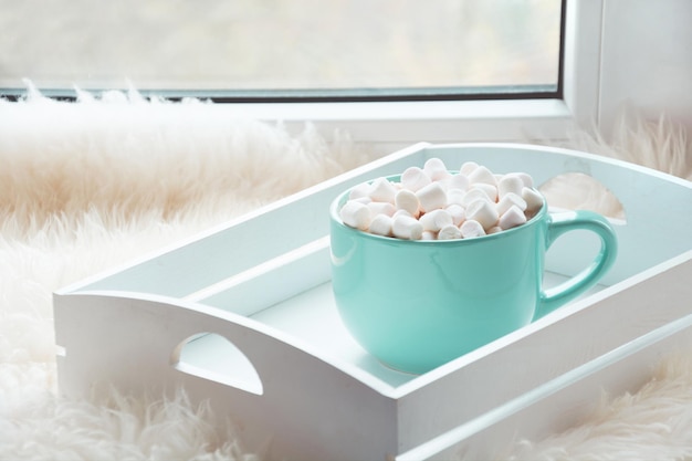 Blaue Tasse heiße Schokolade mit Marshmallow auf der Fensterbank mit Pelzfell-Urlaubskonzept