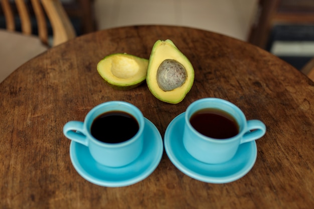 Blaue Tasse heißen schwarzen Kaffees und grüne Avocado.