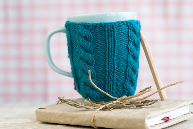 Blaue Tasse in einem blauen Pullover, der auf einem alten Notizbuch steht