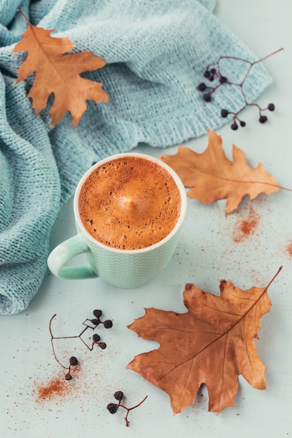 Blaue Tasse Kaffee mit herbstlichen trockenen Blättern und trockenen Beeren auf hellblau