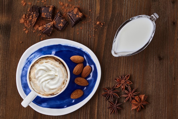 Blaue Tasse Wiener Kaffee mit Sahne, Schokolade und Gewürzen auf einem dunklen Holztisch