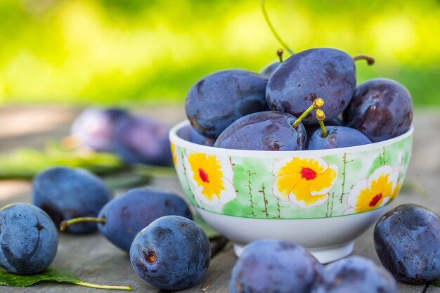 Blaue und violette Pflaumen im Garten auf Holztisch Mehrere frische Pflaumen in einem Retro-Gericht