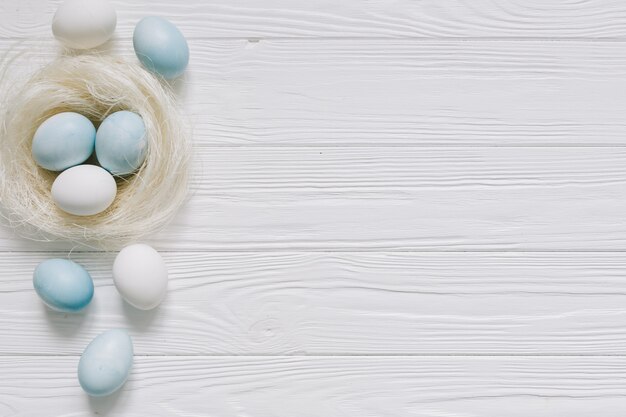 Blaue und weiße Ostereier im Nest auf weißem hölzernem Hintergrund.