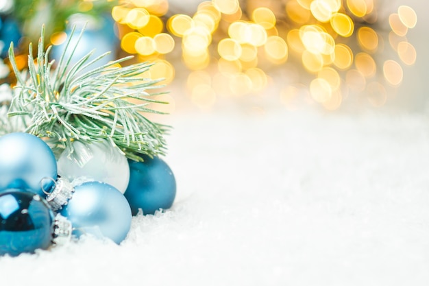 Blaue Weihnachtskugeln und Tannenzweig, die auf dem Schnee auf dem Hintergrund des Weihnachtsbaumes liegen