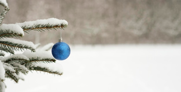 Blauer Ball, Weihnachtsbaumspielzeug, das an einem Weihnachtsbaum in einem verschneiten Winterwald hängt.