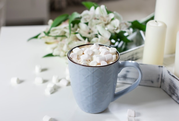 Blauer Becher mit Kakao, Kaffee, Eibische auf weißer Tabelle mit Dekor