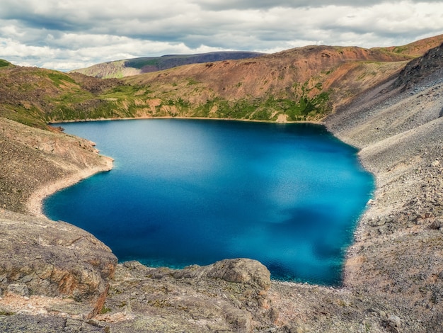 Blauer Bergsee in der Caldera. Gebirgszug gegen einen bewölkten Himmel. Caldera eines erloschenen Vulkans ist von einer Bergkette umgeben. Im Tal befindet sich ein blauer See mit steilen Felsufern.