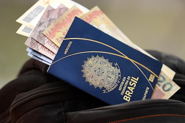 Blauer brasilianischer Reisepass mit Geld und Flugtickets auf einem touristischen Rucksack