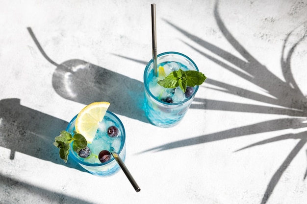 Blauer Cocktail aus Curacao mit frischen Blaubeeren und Zitronenkeilen, garniert mit Minze mit Schatten