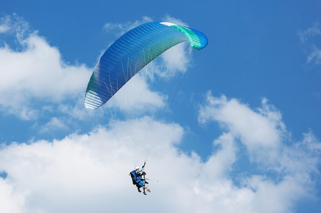 Blauer Gleitschirm, der an einem sonnigen Tag mit Wolken in den Himmel fliegt