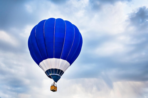 Blauer Heißluftballon, der mit weißen Wolken am blauen Himmel fliegt