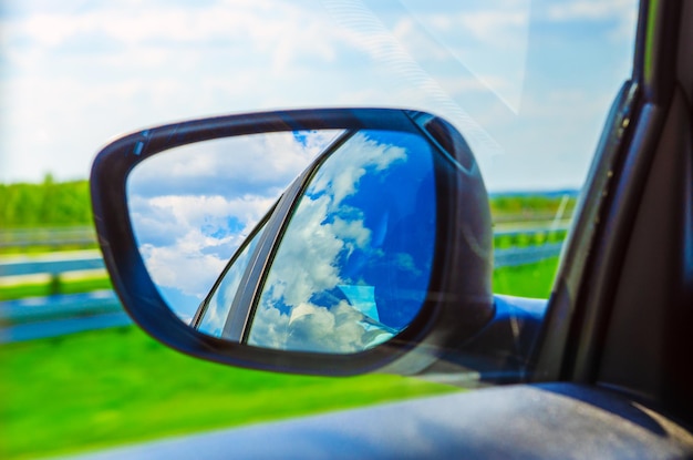 Blauer Himmel mit Wolken im Seitenspiegel eines Autos, auf Straßenlandschaft. Reisen Sie natürliches Abenteuerkonzept