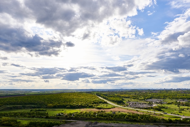 Blauer himmel mit wolken über grünen bäumen und straßen außerhalb der stadt.