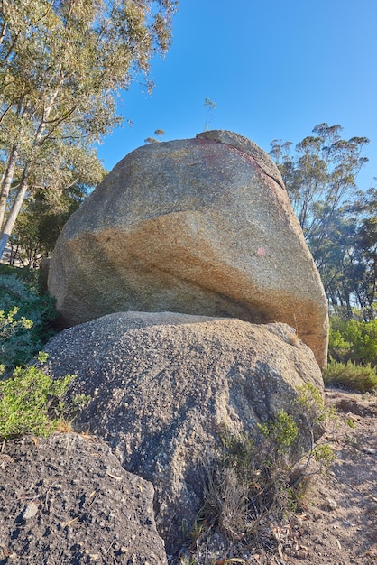 Foto blauer himmel verwitterter felsen und rissiger stein durch hitzeeinwirkung und winderosion entlang eines feldweges auf dem land landschaftsansicht eines weges, der zu üppigen grünen wäldern oder wäldern in einem abgelegenen naturschutzgebiet führt