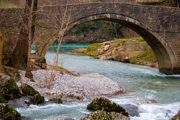 Blauer klarer Fluss mit einem felsigen Ufer unter einer alten Steinbrücke