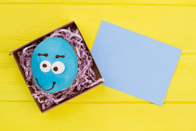 Blauer lustiger Donut im Kasten. Donut in Geschenkbox und leere Papierkarte. Idee zum Geburtstagsgruß.