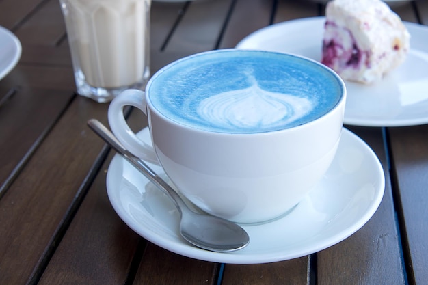 Blauer Matcha-Tee in einer weißen Tasse auf dem Tisch mit Dessert