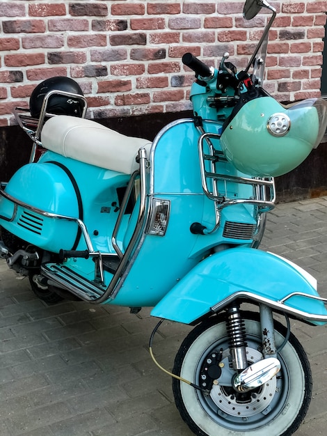 Blauer Retro-Roller mit Helm hängt am Lenkrad, das auf der Straße geparkt ist