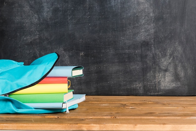 Blauer Rucksack mit Büchern auf Holztisch