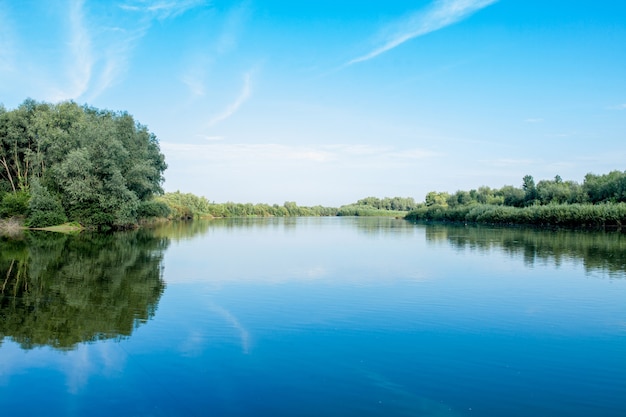 Blauer schöner Himmel vor dem Hintergrund des Flusses. Wolken werden in ruhigem Wasser angezeigt