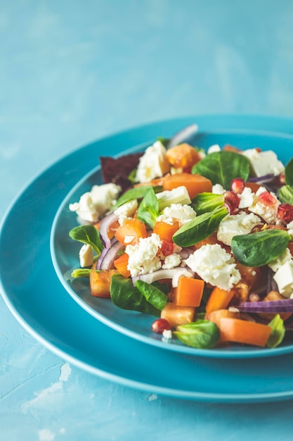 Blauer Teller mit frischen Superfoods, gesundem Salat mit roten Zwiebeln, Tomaten, Doucette-Feldsalat, Maissalat, Feldsalat und Feta-Käse. Hellblaue Oberfläche