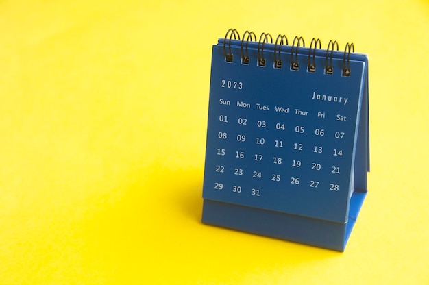 Blauer Tischkalender für Januar 2023 auf gelbem Einbandhintergrund mit anpassbarem Platz für Text, Kopierraum und Kalenderkonzept