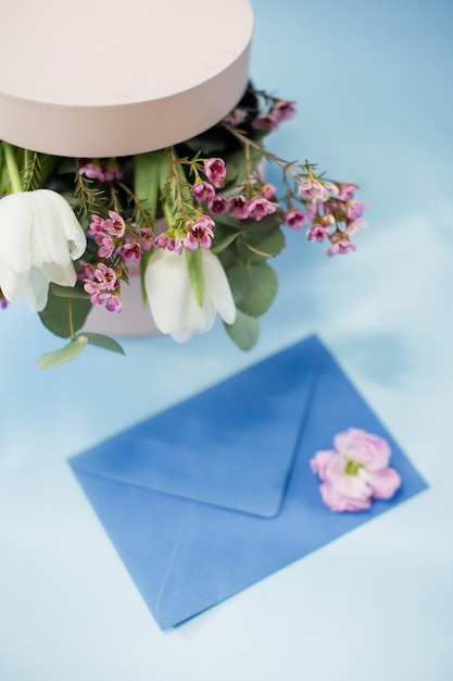 Blauer Umschlag und rosa Geschenkbox mit Blumenstrauß auf blauem Hintergrund