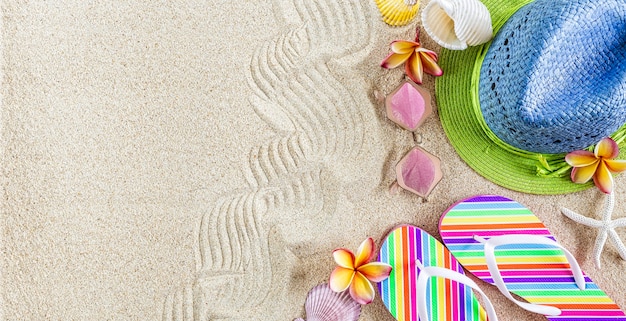 Blauer und grüner Strohhut und bunte Flip Flops im Sand mit Muscheln und Frangipani-Blumen. Sommerzeit am Strandkonzept, Kopierraum