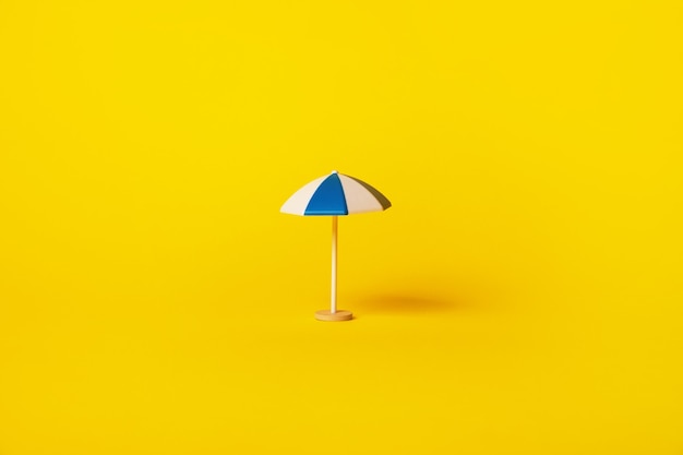 Blauer und weißer Sonnenschirm über gelbem Hintergrund, Urlaubskonzept