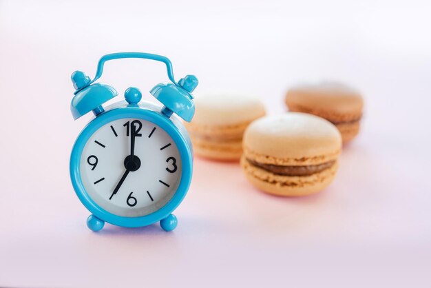 Blauer Wecker und Vanille-Mokka und Schokoladen-Macarons auf rosa Hintergrund