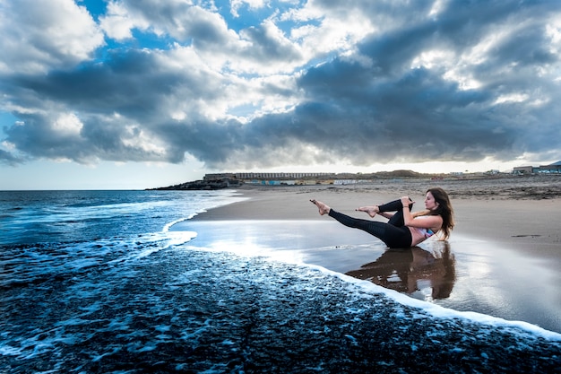 Blaues Bild im epischen Stil mit hübscher Brünette beim Sport und Pilates-Aktivität am Strand am Ufer