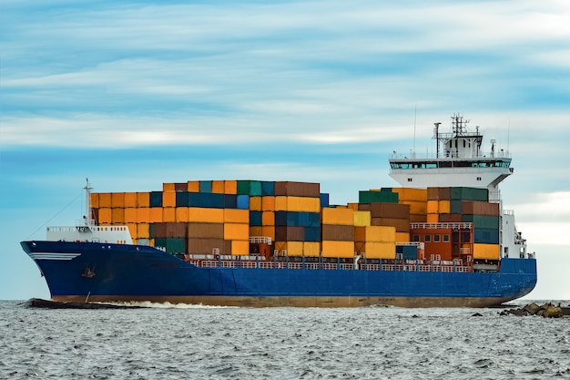 Blaues Containerschiff voll beladen vom Meer bewegend